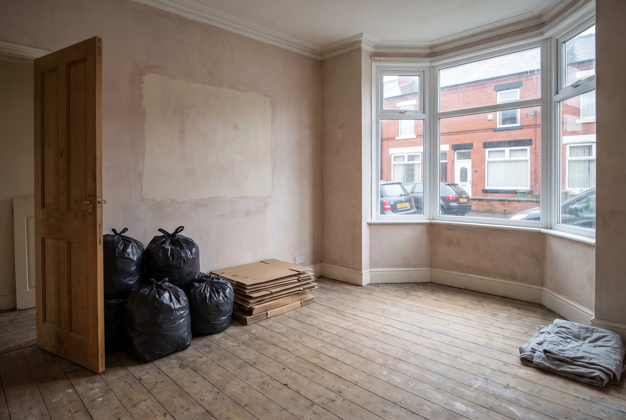 An emptied room with bare floorboards and tied sacks and flattened boxes stacked by the door