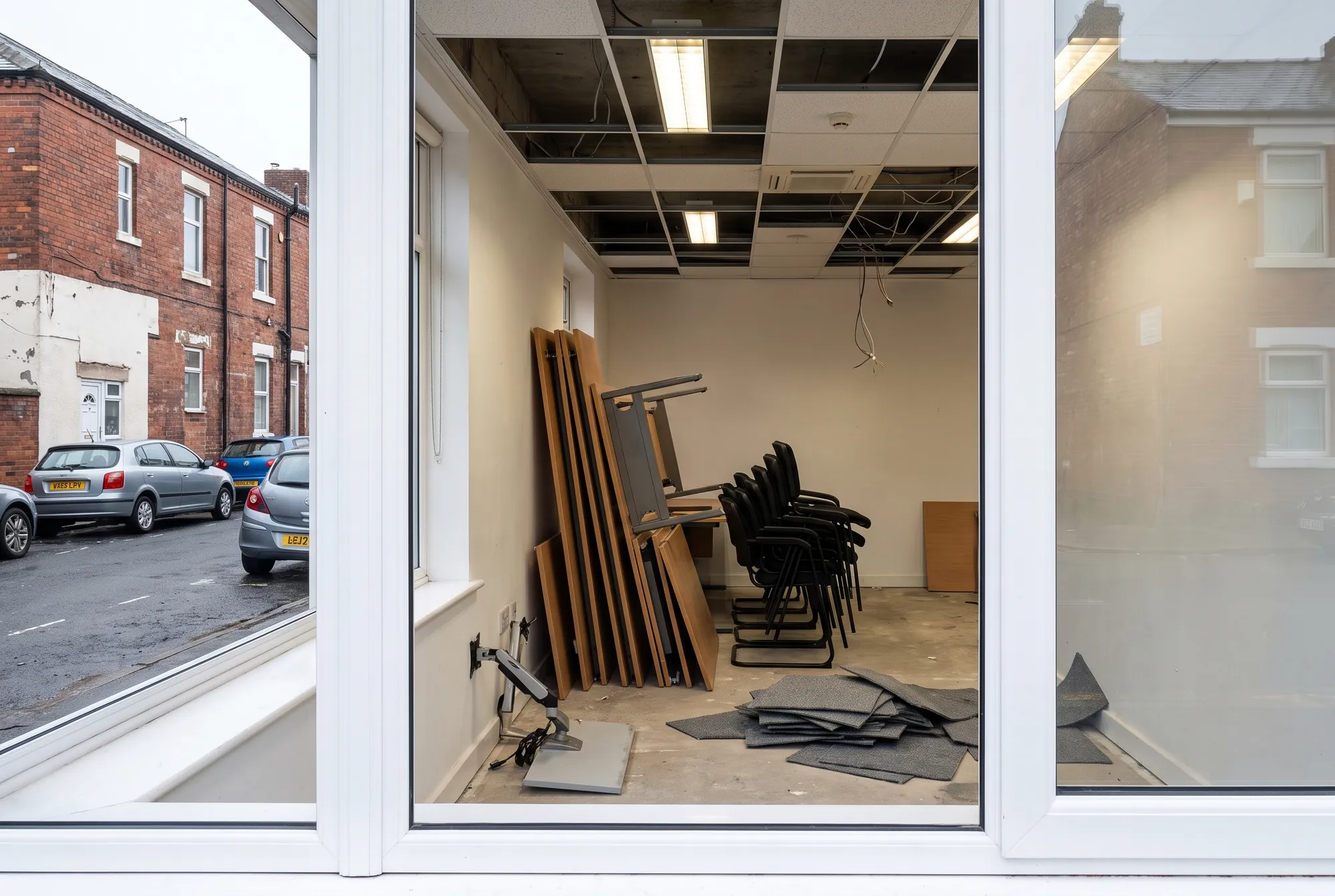 A stripped office floor with desks stacked on their sides, chairs nested and carpet tiles lifted